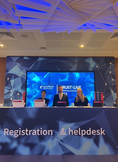 Two women and a man smiling and standing behind a tradeshow registration and help desk