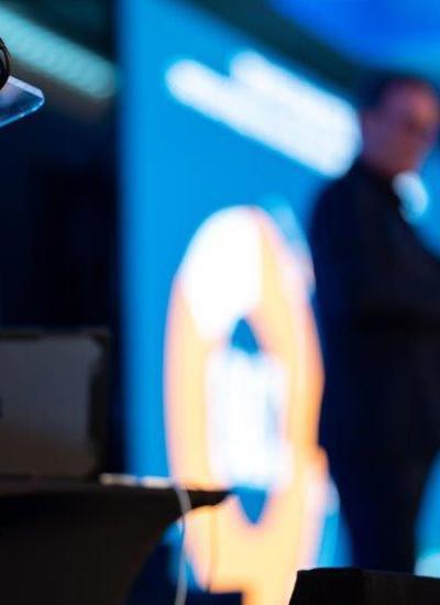 A lectern with a sign reading LNRS Trust Live and in the background a person speaking on a stage