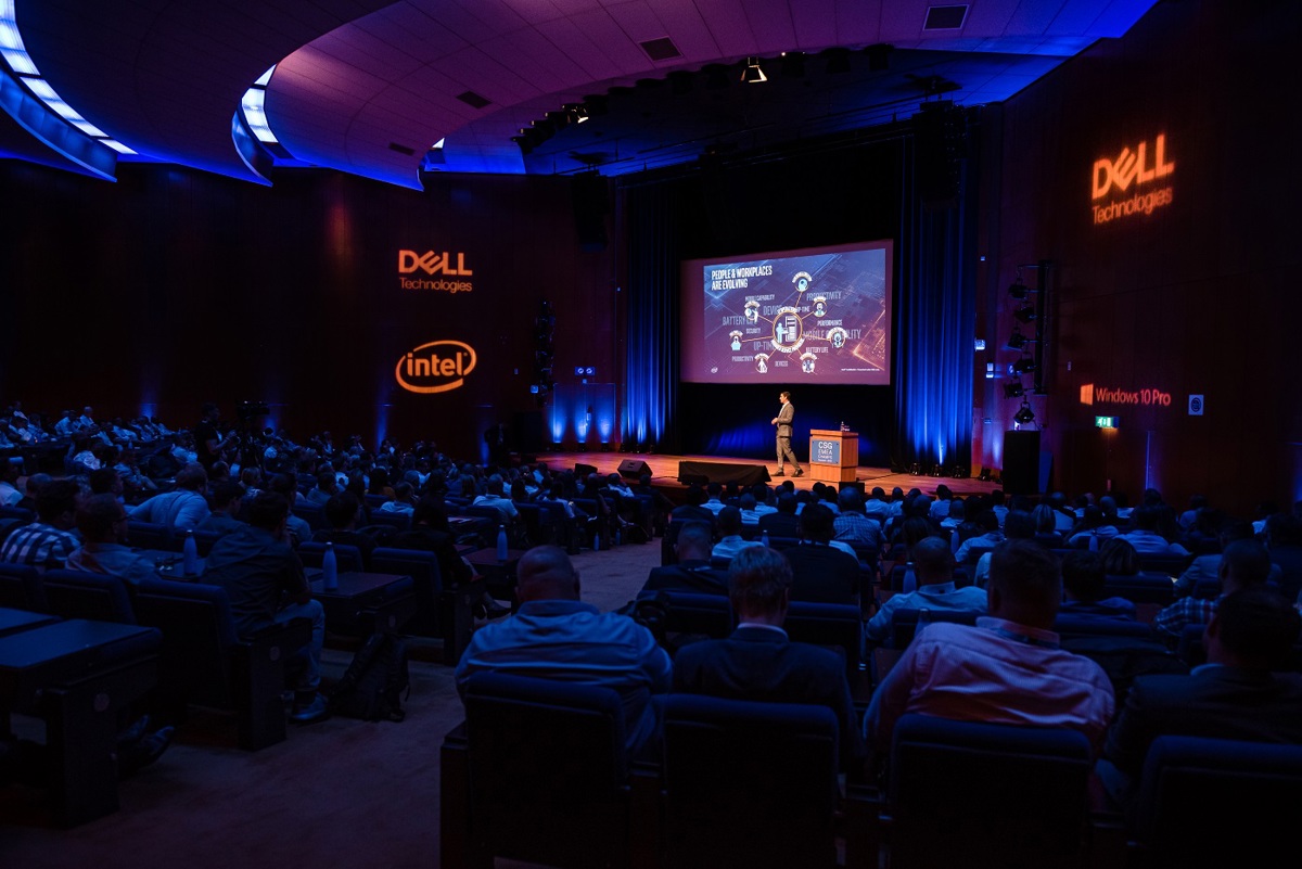 A room full of seated people watching a presentation given by a person on a stage with Dell and Intel signage