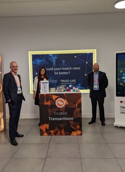 Three people standing next to a tradeshow booth called Trusted Transactions