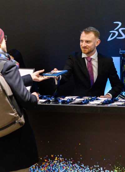 A man in a black suit is handing something to a person wearing a hat at a registration desk