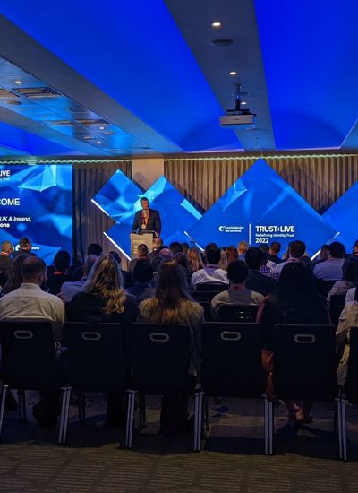 A room full of seated people watching a presentation given by a person on a stage