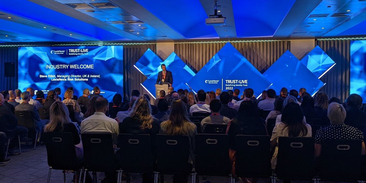 A room full of seated people watching a presentation given by a person on a stage