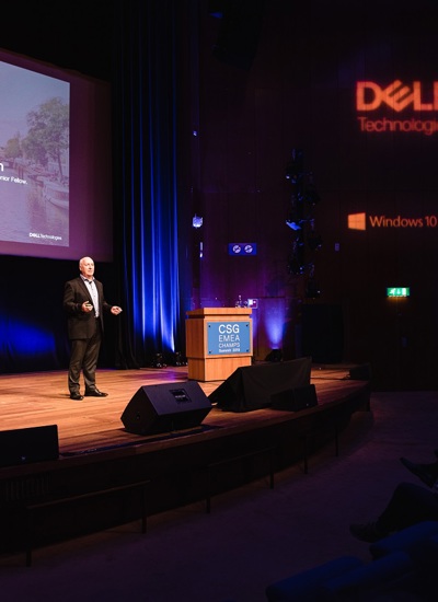 A room full of seated people watching a presentation given by a person on a stage